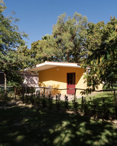 Bungalow giallo con porta rossa, giardino.