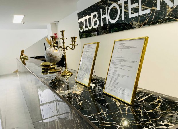 Reception con bancone in marmo nero, candelabro e documenti incorniciati.