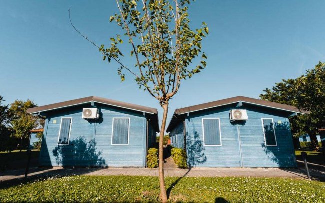 Due bungalow blu affiancati, con un albero davanti e cieli blu chiaro.