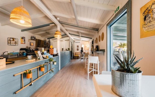 Interno di un bar luminoso con bancone, sgabelli e decorazioni aeree.