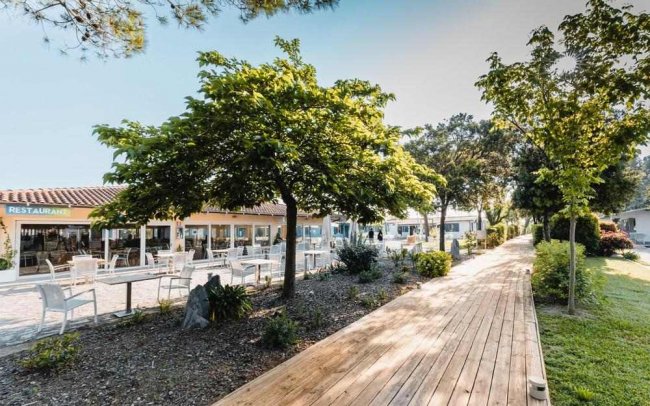 Un sentiero pedonale in legno accanto a un ristorante con tavoli all'aperto e alberi ombreggianti.