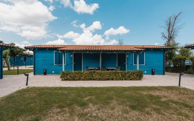 Edificio blu con tetto in tegole, circondato da siepi e un vialetto pavimentato.