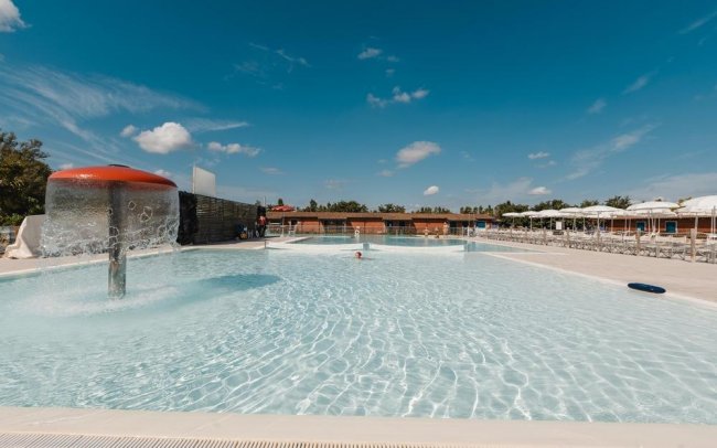 Piscina con fontana a fungo, sdraio e cielo sereno con alcune nuvole.