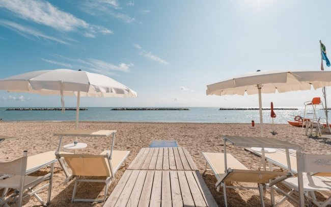 Spiaggia sabbiosa con ombrelloni bianchi e lettini, mare e cielo limpido all'orizzonte.