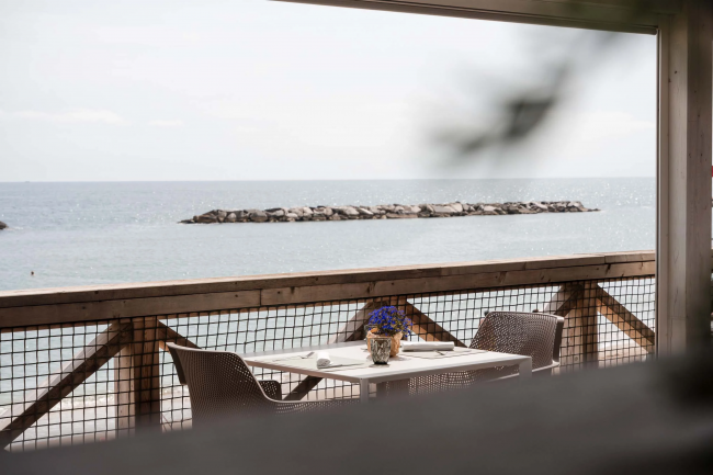 Tavolo per due sul mare con fiori al centro e barriera rocciosa sullo sfondo.