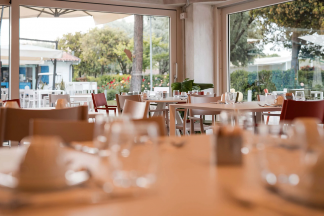 Ristorante con ampie finestre, tavoli apparecchiati e vista sul giardino.