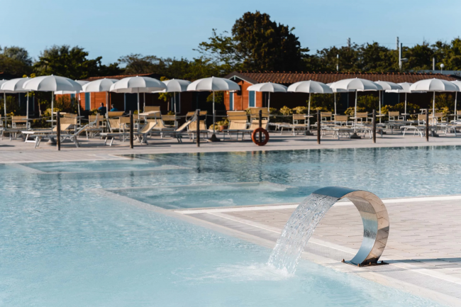 Piscina con cascata d'acqua, lettini e ombrelloni bianchi.