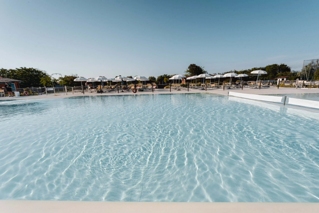 Una piscina scintillante sotto un cielo azzurro con ombrelloni bianchi sullo sfondo.