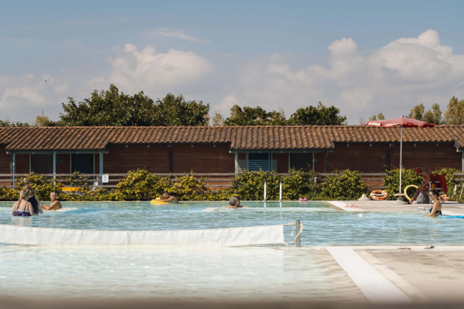 Persone rilassate in piscina all'aperto con edifici di legno sullo sfondo.