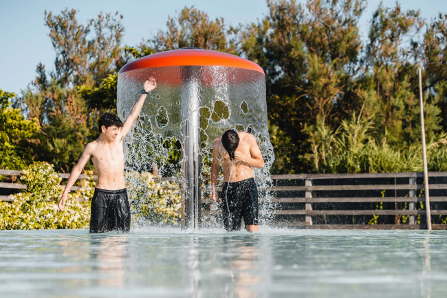 Due ragazzi giocano sotto una fontana a forma di fungo in piscina.