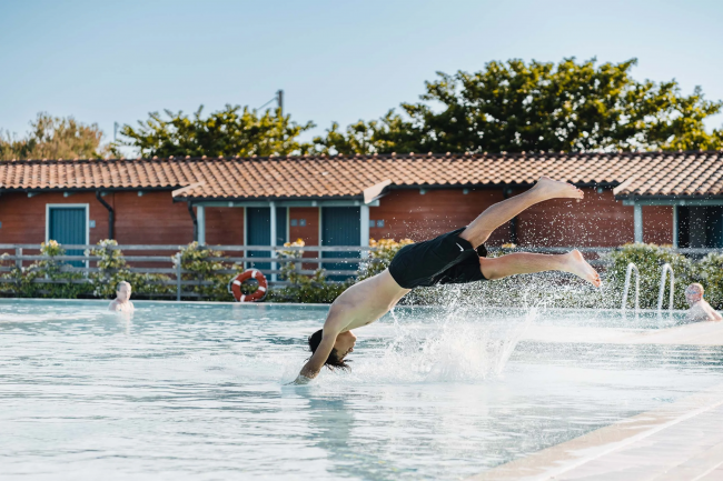 Ragazzo si tuffa in piscina vicino a edifici di legno.