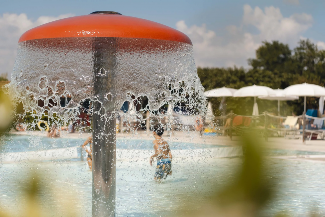 Una fontana a forma di fungo in una piscina con bambini che giocano attorno.