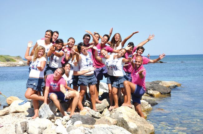 Gruppo di persone sorridenti su rocce vicino al mare.