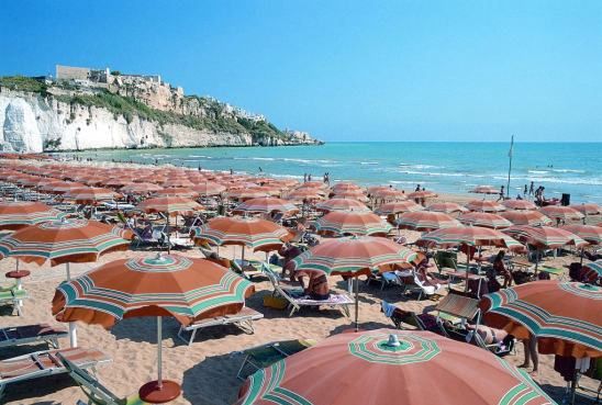Una spiaggia affollata con ombrelloni arancioni e vista di scogliere sullo sfondo.