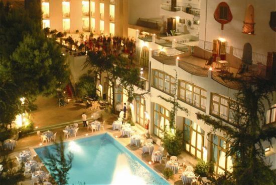 Piscina notturna circondata da tavoli apparecchiati e un edificio illuminato.