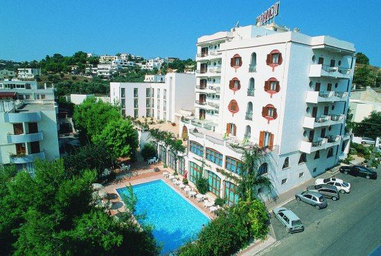 Un hotel bianco a cinque piani con una piscina blu e giardini verdi.