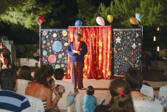 Uno spettacolo di clown all'aperto, con tende rosse e pubblico seduto su sedie.