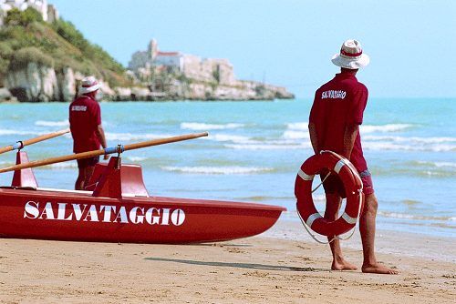 Due bagnini con divisa rossa e cappelli bianchi su una spiaggia sabbiosa vicino al mare.