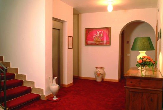 Interno di un edificio con moquette rossa, un'ascensore, scale e mobili in legno.