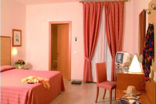 Camera da letto con tenda rossa, letto matrimoniale, sedia, scrivania e televisore.