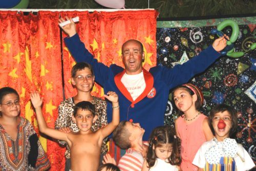 Gruppo di bambini e un uomo sorridente davanti a una tenda colorata.