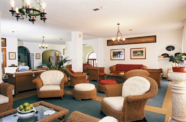Sala con sedie e divani di vimini, decorata con quadri e lampadari.