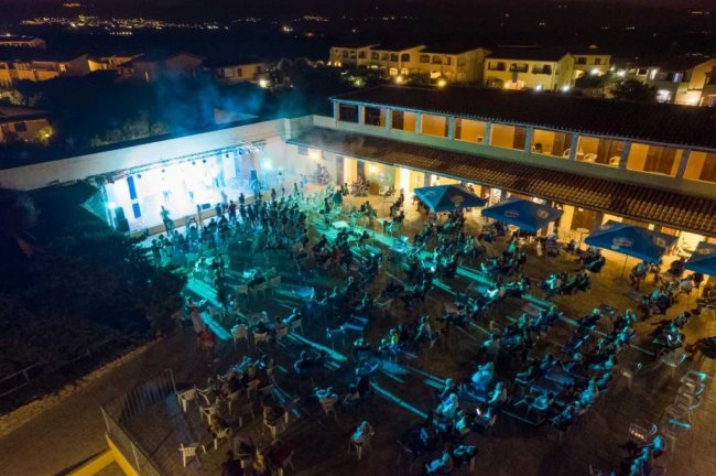 Evento serale all'aperto, folla illuminata da luci blu.