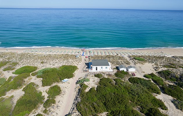Vista aerea spiaggia con ombrelloni e mare blu.