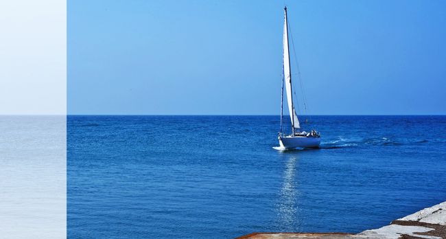 Una barca a vela bianca solca il mare blu sotto un cielo limpido.