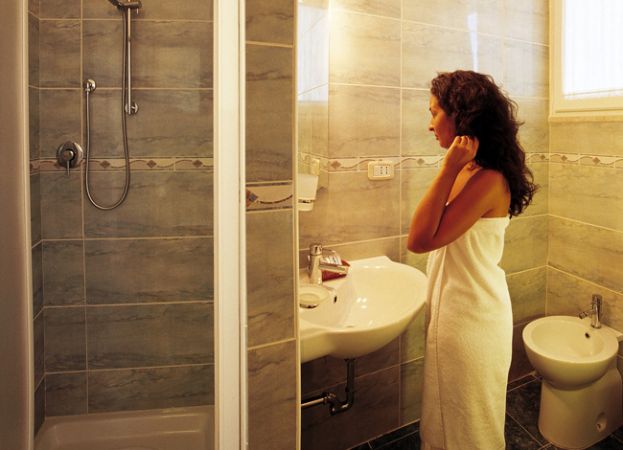 Una donna avvolta in un asciugamano si guarda nello specchio di un bagno moderno con doccia.