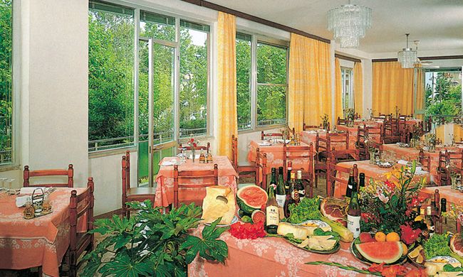 Sala da pranzo con tavoli imbanditi e vista su giardino.