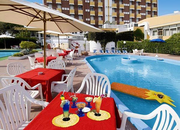 Piscina con tavoli rossi e cocktail colorati su prato.