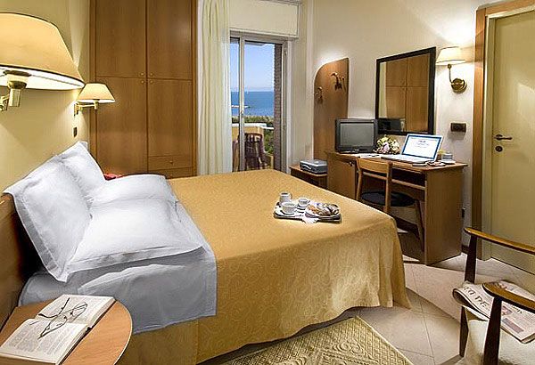 Una camera d'hotel con letto matrimoniale, vista mare e scrivania con computer.