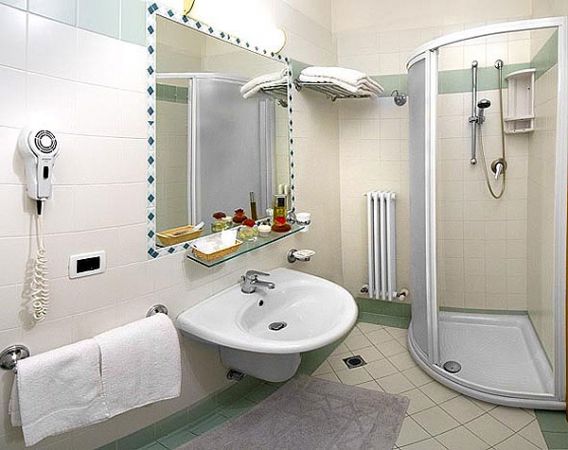 Bagno con doccia angolare, lavabo, specchio e asciugacapelli a parete.