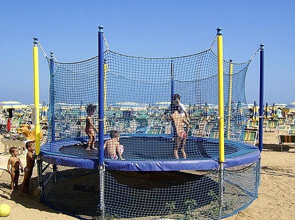 Bambini giocano su un trampolino elastico su una spiaggia soleggiata.