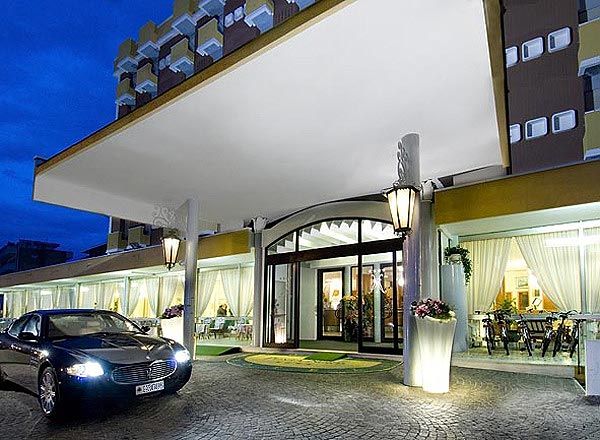 Ingresso di un hotel con tettoia bianca e un'auto parcheggiata davanti.
