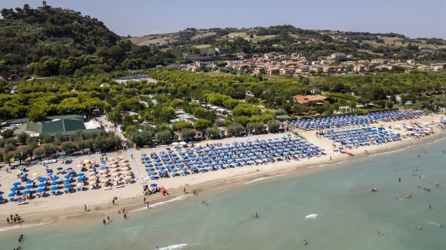 Lunga spiaggia con ombrelloni e colline sullo sfondo.