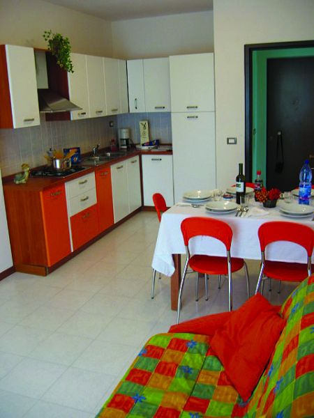 Cucina colorata con tavolo apparecchiato e sedie rosse, divano con cuscini.