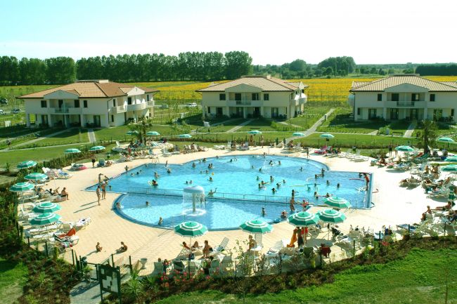 Ampia piscina circondata da sdraio e villette, immersa nel verde.