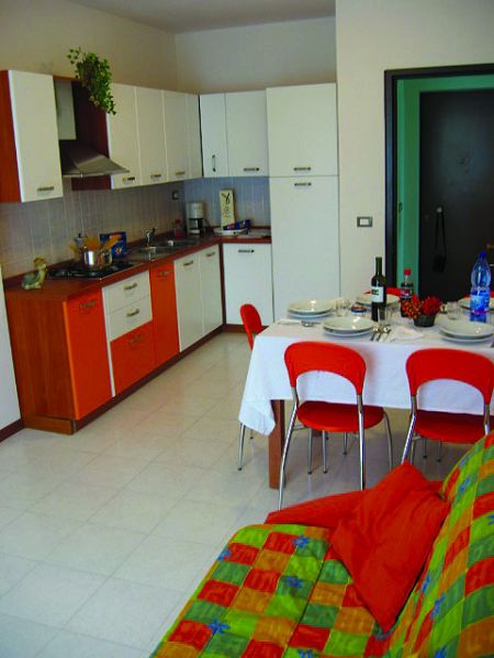 Cucina moderna con tavolo apparecchiato, sedie rosse e divano colorato.