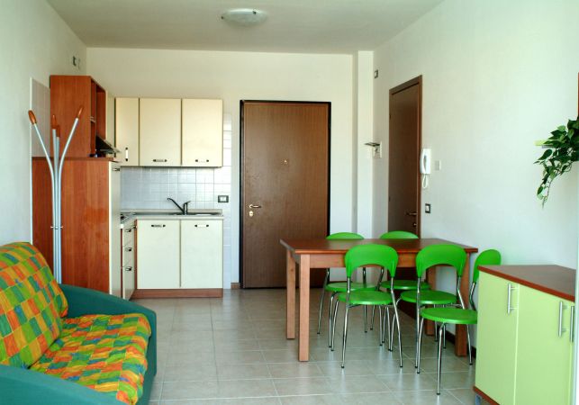 Una stanza con cucina, tavolo e sedie verdi, divano verde e giallo.