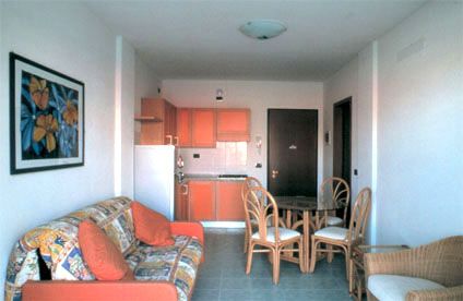 Soggiorno con divano arancione, tavolo e sedie in legno, e quadro floreale.