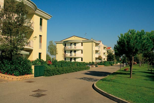 Complesso residenziale con giardini e strada pedonale, cielo blu.
