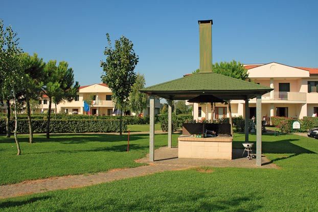 Un'area barbecue coperta con prato e case sullo sfondo.