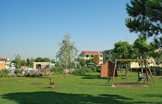 Un parco giochi con altalene, prato verde, e case in lontananza.