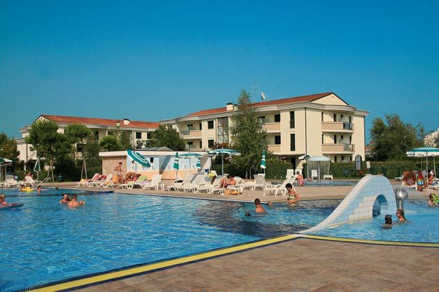 Una grande piscina con scivoli, lettini e persone che si godono il sole.
