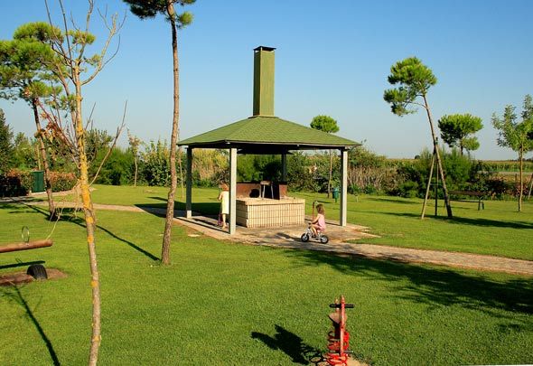 Giardino verde con tettoia, barbecue e due bambini; uno va in bici.