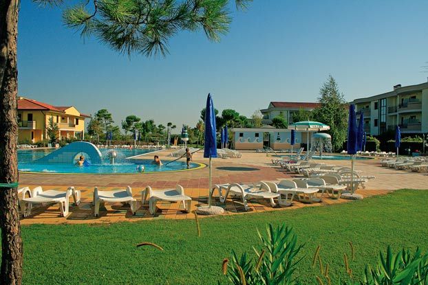 Piscina all’aperto con sdraio e ombrelloni blu e edifici sullo sfondo.