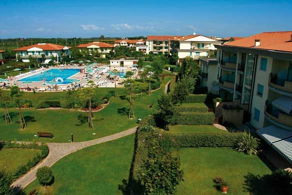 Complesso residenziale con piscina e giardini curati, visti dall'alto, in una giornata soleggiata.