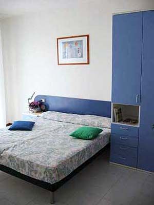 Camera da letto minimalista con letto matrimoniale, armadio blu e quadro sulla parete.